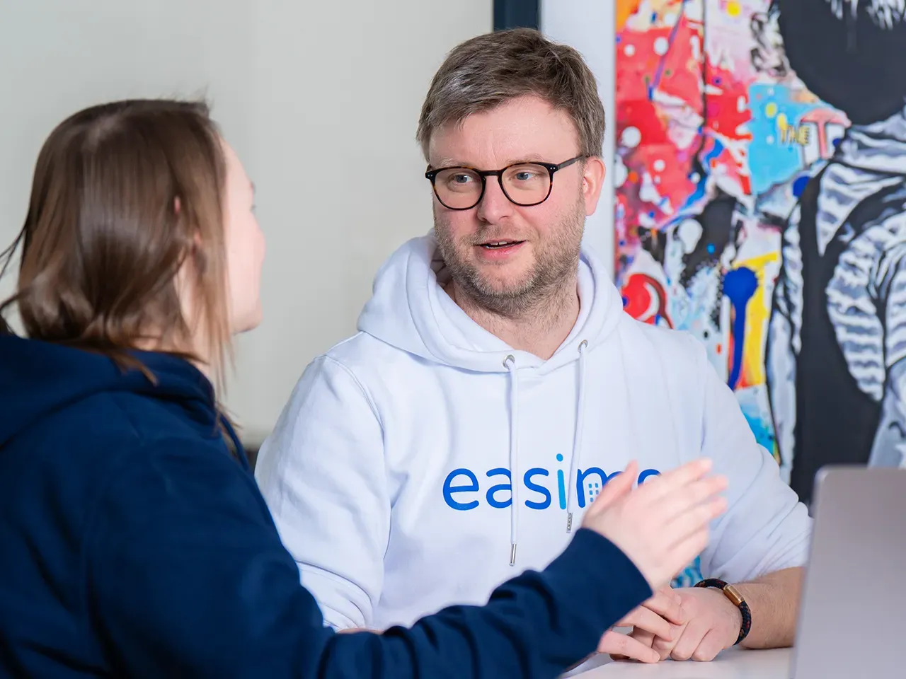 Beratung bei easimo: Zwei Personen sprechen am Arbeitsplatz über individuelle Softwarelösungen für die Immobilienverwaltung.