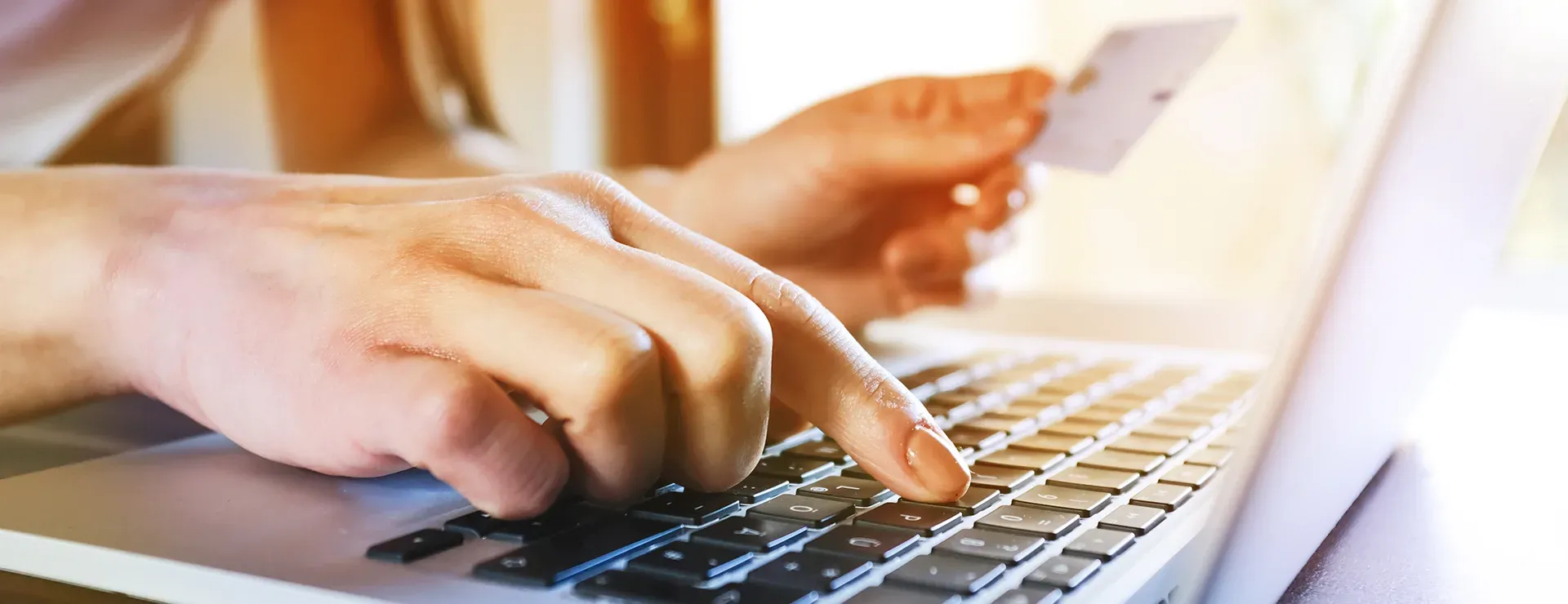 Person gibt Zahlungsdaten am Laptop ein und hält eine Bankkarte in der Hand.