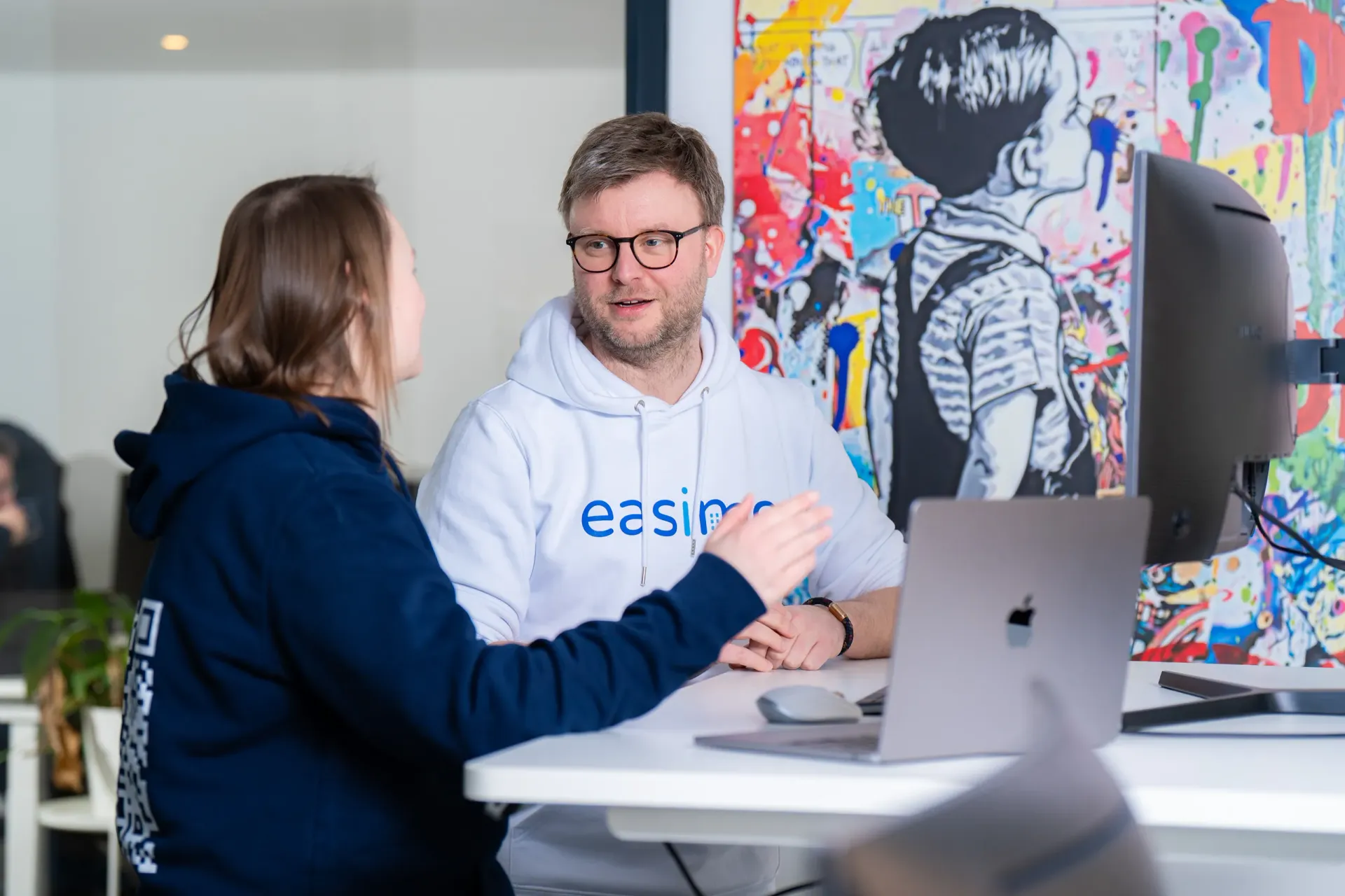 Sales-Team von easimo bei der Kundenberatung: zwei Mitarbeitende sprechen an einem Büroarbeitsplatz über Immobilienverwaltung und Softwarelösungen.