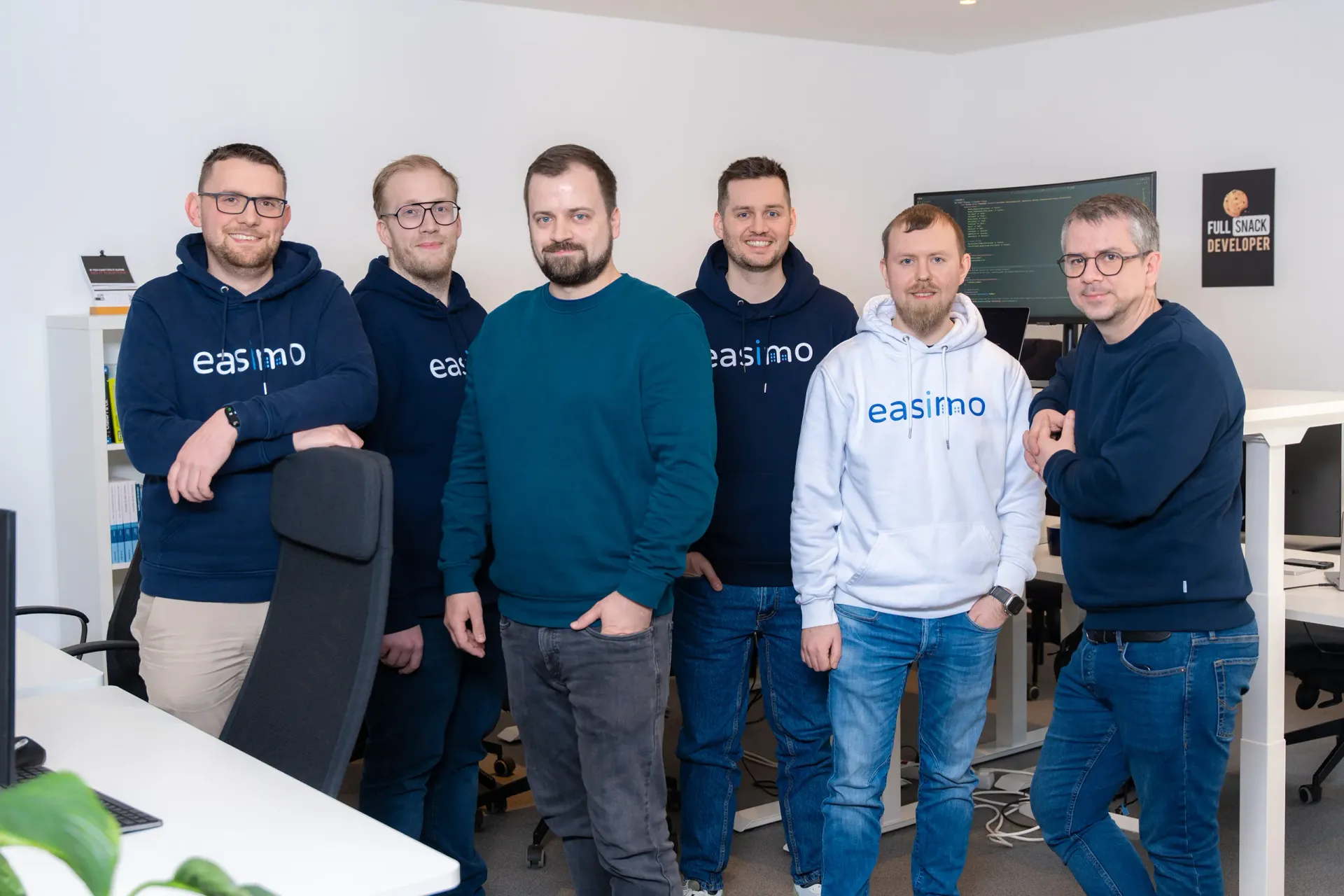 Development-Team von easimo im Büro: sechs Mitarbeitende der webbasierten Immobilienverwaltungssoftware stehen vor Arbeitsplätzen und Monitoren.
